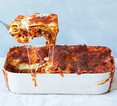 someone is taking a slice of lasagna out of the casserole dish