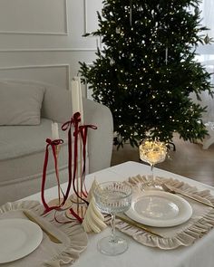 a christmas tree is in the background behind a dining room table with white plates and silverware