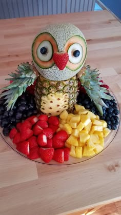 an owl made out of fruit is sitting on a plate with grapes, pineapples and strawberries