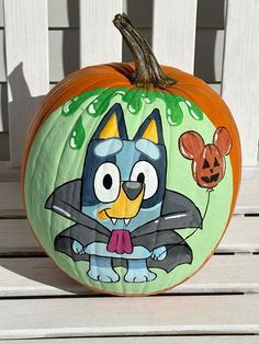 a cartoon character painted on a pumpkin sitting on a wooden bench in front of a white fence