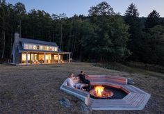 two people sitting around a fire pit in front of a house