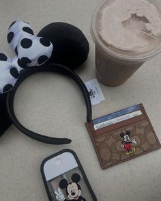 a mickey mouse ears headband, wallet and cell phone on a table next to a cup of coffee