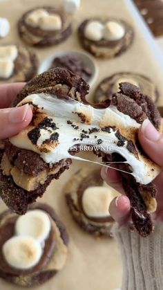 a person holding up a chocolate cookie with white frosting and bananas on it in front of other cookies