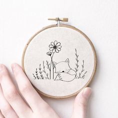 a hand is holding up a embroidery hoop with a fox and flower on it