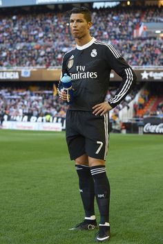 a man standing on top of a soccer field holding a ball in his hand and wearing a black uniform