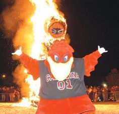 the mascot is standing in front of a large fire with his arms out and hands up