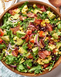 a salad with bacon, avocado, corn and tomatoes in a wooden bowl