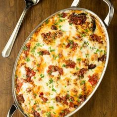 a casserole dish with meat and cheese in it on a wooden table next to two silver spoons