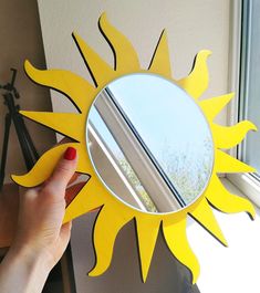 a hand holding a mirror with a yellow sun design on it