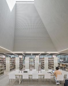 a person sitting at a table in a library with lots of books on the shelves