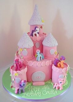 a pink birthday cake decorated with little ponys and princess's castle on top