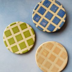 three different colored cookies sitting on top of a blue tablecloth covered surface with white and green designs