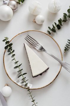 a piece of cheesecake on a plate with silverware and greenery around it