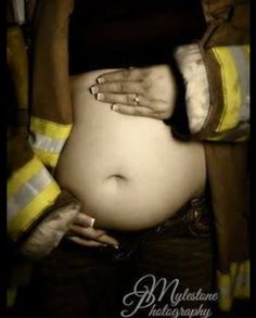 a pregnant woman wearing fireman's gear with her hands on her belly and holding the jacket over her stomach