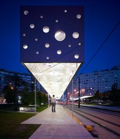 a man walking down a sidewalk next to a tall building with lots of lights on it