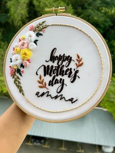 a hand holding up a embroidery hoop with the words happy mother's day on it