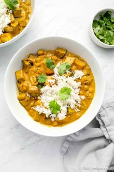 two bowls filled with curry and rice on top of a white countertop next to a bowl of cilantro