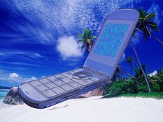 an open cell phone laying on top of a sandy beach next to the ocean and palm trees