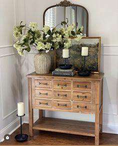 a wooden dresser with flowers and a mirror on the top shelf next to a candle