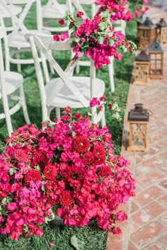 rows of white chairs with pink flowers and lanterns in the grass on either side of them