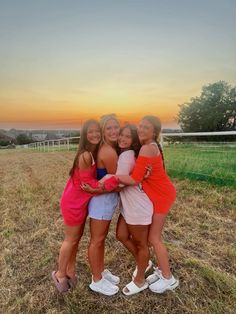 three girls hugging each other in the middle of a grassy field at sunset with an ocean in the background