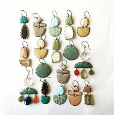 a collection of earrings hanging from hooks on a white wall in various shapes and sizes