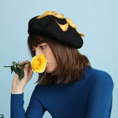 a woman wearing a black hat and holding a yellow rose in front of her face