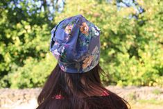 a woman with long hair wearing a blue floral print hat and looking at the trees