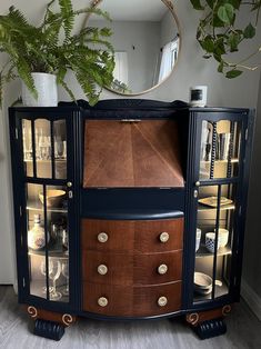 a blue cabinet with glass doors and gold knobs on the bottom, next to a potted plant