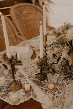 a table topped with candles and flowers on top of a lace covered table cloth next to two vases