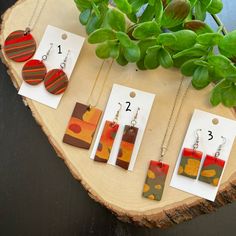 four different necklaces are displayed on a piece of wood next to some green plants