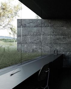 an empty desk in front of a large window with grass on the outside and trees behind it