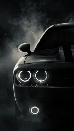 a black and white photo of a car with fog coming from the hood, lights on