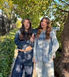 two young women standing next to each other on a sidewalk in front of a tree