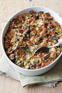 a white bowl filled with food sitting on top of a wooden table next to a spoon