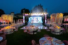 an outdoor event set up with tables, chairs and lights on the grass at night