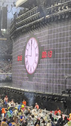 a large group of people standing in front of a giant screen with a clock on it