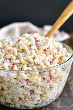 a glass bowl filled with macaroni salad on top of a wooden cutting board