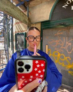 a woman in glasses is holding a cell phone case with stars on it and drinking from a straw