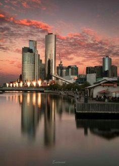 the city skyline is reflected in the water at sunset, with pink and purple clouds