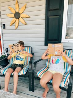 two people sitting on lawn chairs holding up boxes in front of their faces while reading books