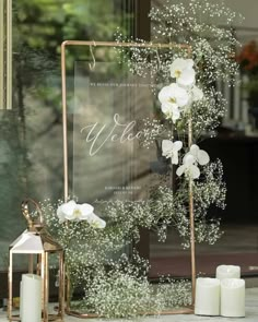 white flowers and baby's breath are displayed in front of a glass sign that says welcome