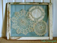 an old frame with lace doily on it in front of a white wall hanging