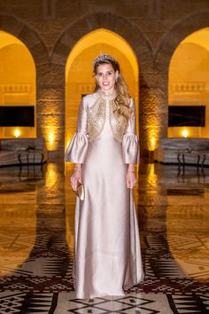 a woman in a long dress standing on a tile floor wearing a tiara and holding a purse