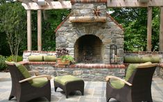 an outdoor fireplace with wicker chairs and green cushions in front of it on a stone patio