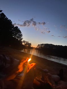 people are sitting on the beach at sunset with a candle in their hands, and one person is laying down