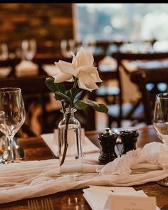 the table is set with wine glasses, napkins and a flower in a vase