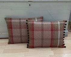 two plaid pillows with pom - poms on them