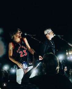 two men singing into microphones in front of a crowd