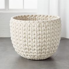 a large white woven basket sitting on top of a cement floor next to a window